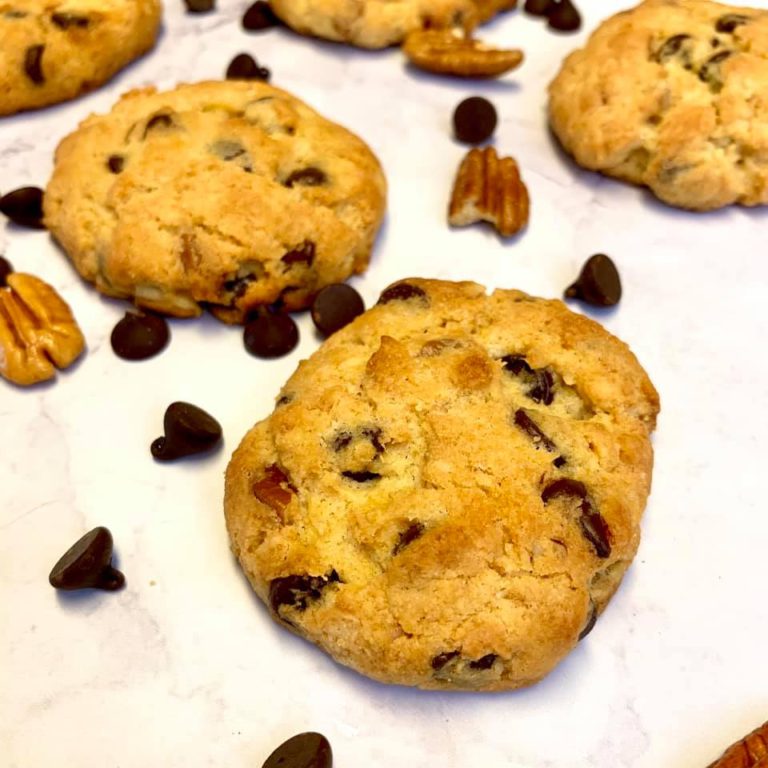 Low carb chocolate chip pecan cookies on a table with pecans and chocolate chips next to the cookies
