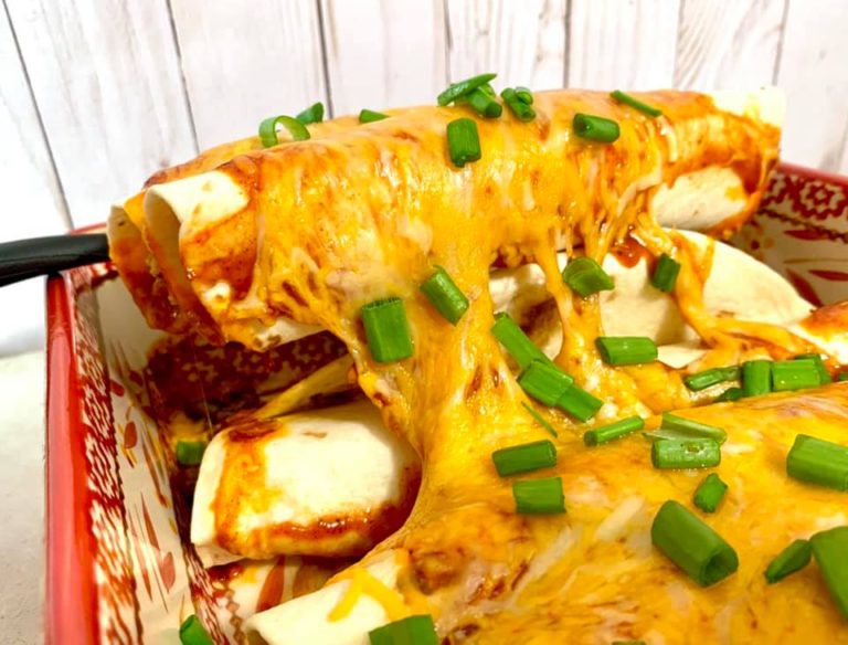 melted cheese and diced green onions on enchiladas in a red and white baking pan