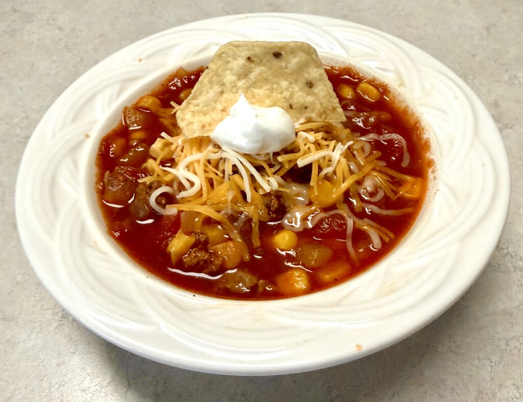 white bowl of taco soup topped with cheese and sour cream