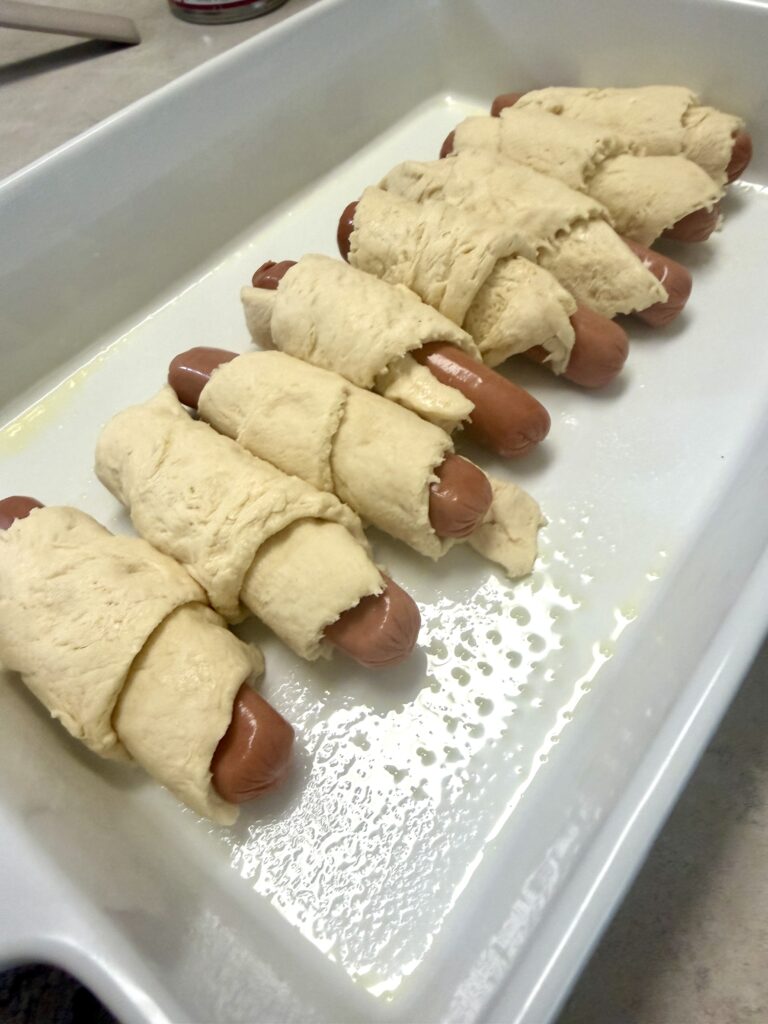 Picture of a 4 ingredient chili cheese hotdog bake in a white baking dish.