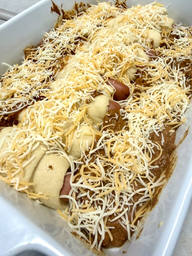 Picture of a 4 ingredient chili cheese hotdog bake in a white baking dish.