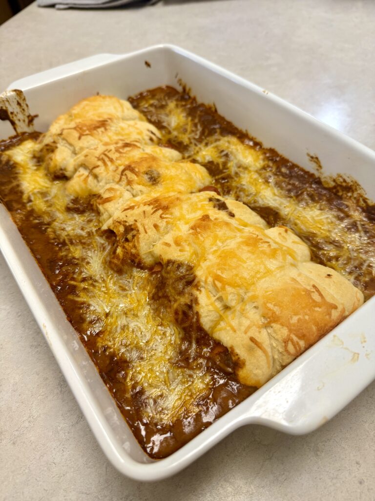 Picture of a 4 ingredient chili cheese hotdog bake in a white baking dish.