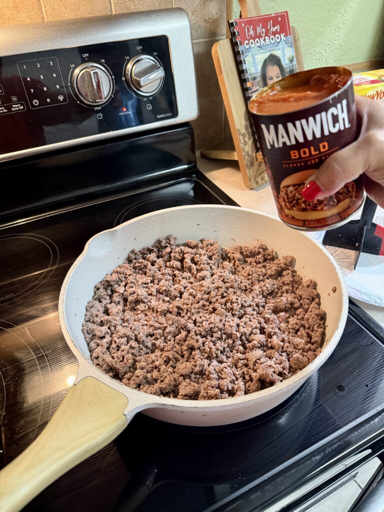 Picture of cooked ground beef in a white skillet and a can of Manwich sloppy joe sauce.