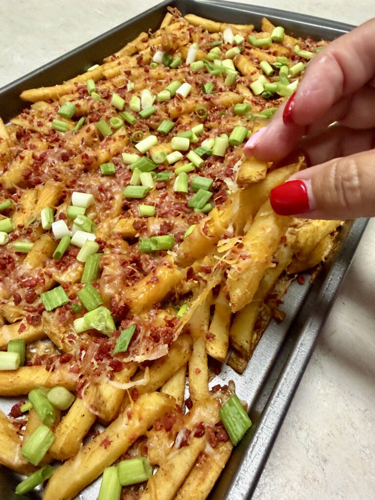 a hand holding some bacon cheesy french fries