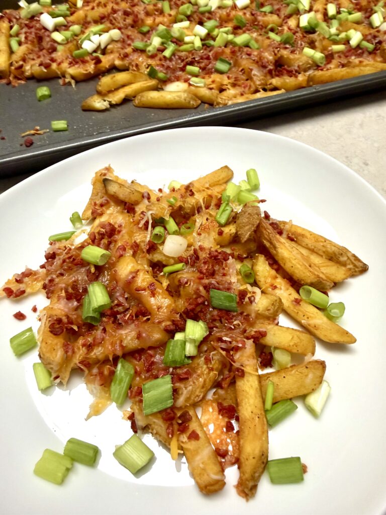 bacon cheese fries on a white plate and a baking sheet