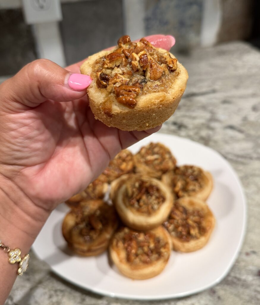 a hand holding pecan pie tarts